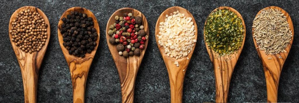 Various spices like coriander, black pepper, and rosemary displayed on wooden spoons, representing agricultural trading and spice supply